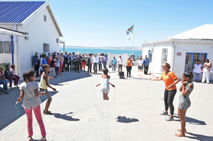 Kinder in Paternoster spielen mit Praktikantinnen und Praktikanten. Im Hintergrund ist die Delegation um Wissenschaftsministerin Theresia Bauer zu sehen. Foto: Stiftung Kinder fördern – Zukunft stiften.